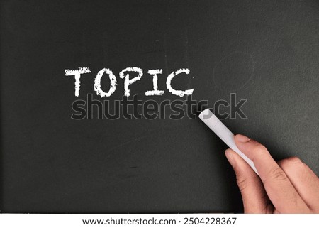 text of TOPIC with hand holding chalk on black board and school tools and stationeries for EDUCATION conceptional. 