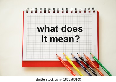 text what does it mean written on notepad with pencils and white background. High quality photo