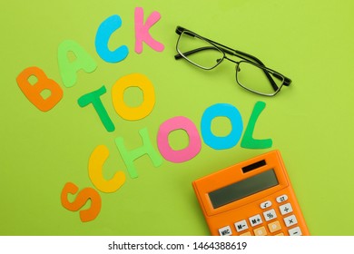 The text will be returned to the school from multicolored letters and glasses and a calculator on a bright green background. Office tools. education. top view.