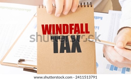 Text WINDFALL TAX on brown paper notepad in businessman hands on the table with diagram. Business concept