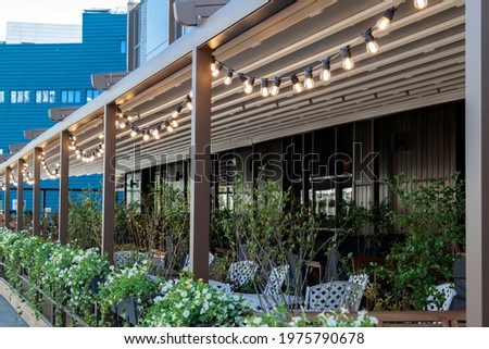 textile awning with metallic frame and edison pendant lamps glowing with warm light on terrace of street cafe, nobody