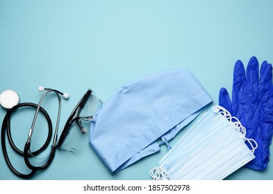 Textile Blue Cap, Disposable Medical Mask, Pair Of Gloves And Plastic Glasses On A Blue Background, Top View. Medic Protective Clothing