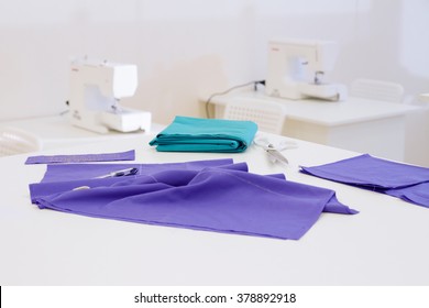 Textile On White Table In The Sewing Workshop Room With Sewing Machines On Background