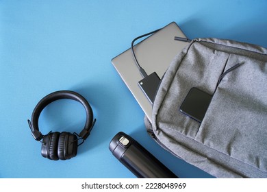Textile urban backpack with laptop, external SSD, smartphone, headphones and thermos. Traveling with gadgets. Pre-flight screening. Hand luggage in airport. Carry liquid on board aircraft. Close-up