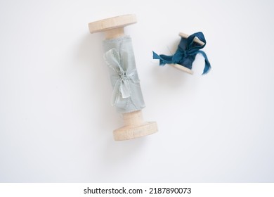Textiles For The Holiday. Wedding Decoration Element, Light Blue Silk Ribbon Next To Small Blue Ribbon On Wooden Role Lies On White Background