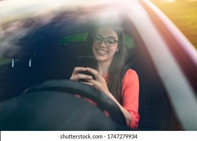 Texting And Driving, Behind The Wheel. Breaking The Law. Woman Driving Car Distracted By Her Mobile Phone. Woman Typing Message On The Phone While Waiting In The Car.