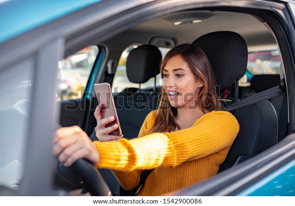 Texting and driving, behind the\
wheel. Breaking the law. Woman driving car distracted by her mobile\
phone. Woman typing message on the phone while waiting in the\
car.