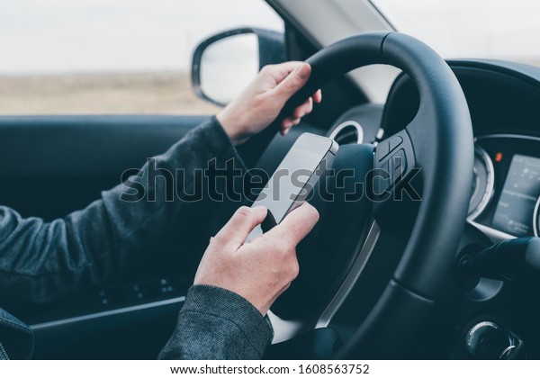 Texting and driving is dangerous\
behavior in traffic, close up of female hand typing text message on\
mobile phone while traveling through countryside with her\
car