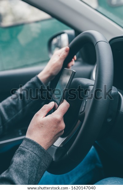 Texting and driving is dangerous\
behavior in traffic, close up of female hand typing text message on\
mobile phone while traveling through countryside with her\
car