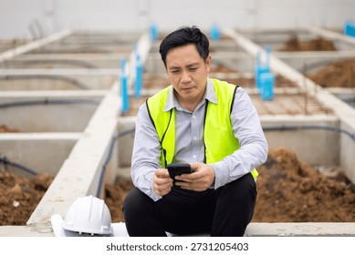 texting on cell phone while relaxing. Civil engineer Asian man in safety hard hat helmet working at construction site