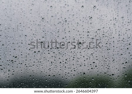 Textural image of a rainy window pane, showcasing various sizes of water droplets and a muted, out-of-focus green landscape beneath.
