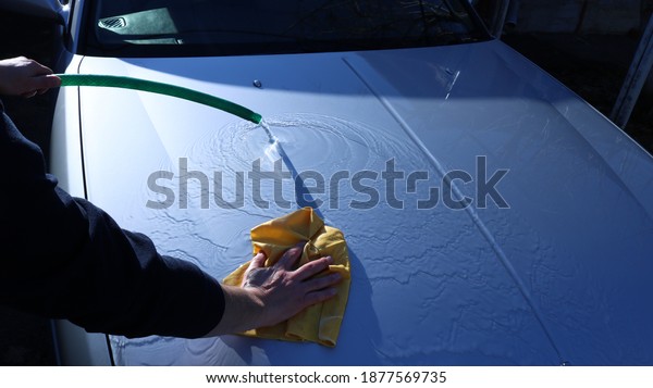 textural movement of water on a clean hood of a gray\
car during washing by hand using a hose and a suede cloth to clean\
the vehicle from light\
dirt