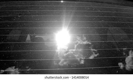 Texture, background, image, of the reflection of the sun and the sky with clouds on the rear tinted window of the car with stripes and dust, reminiscent of the night starry sky in black and white.
