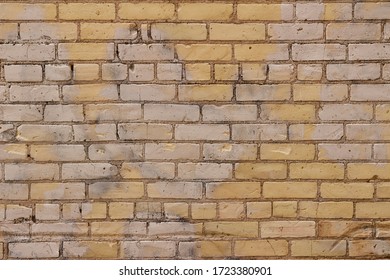 Texture background of an old grungy yellow brick wall with random faded white paint in patchy areas