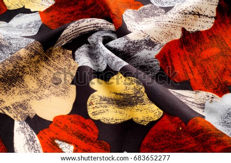 Texture, background, pattern. A woman's silk handkerchief is decorated with bright colors. White yellow red flowers on a black background