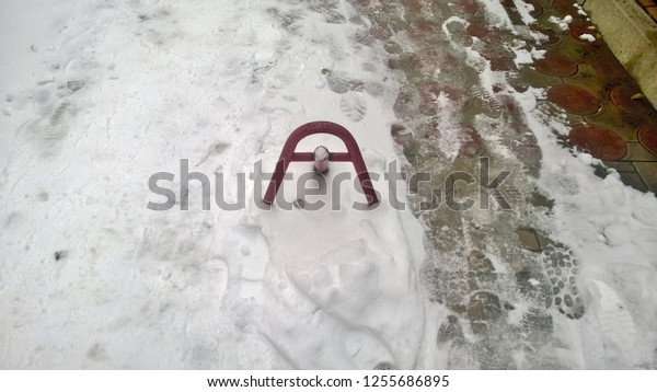 Texture and background\
of a red blocker for cars, people trodden paths on the snow on the\
street in the afternoon in the winter. Human footprints from shoes.\
White snow.