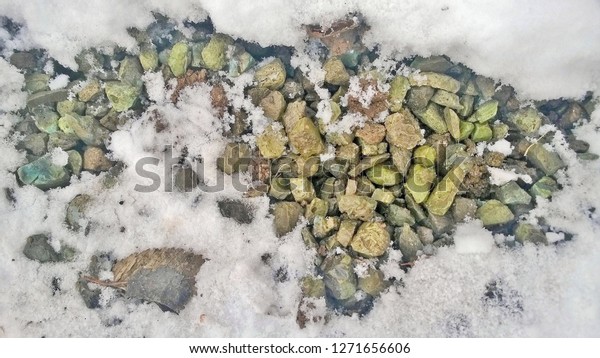 Texture, background,\
wallpaper of white snow and ice with tracks of cars, people, human\
footwear on a pile of stones, gravel in the middle of a winter day\
on the street.