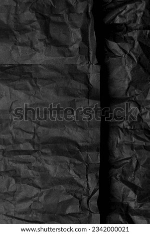 Texture of black crumpled paper. Dark paper background with chaotic bends. A sheet of black wrinkled paper