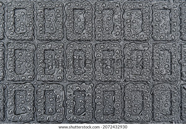 The texture of a black\
rubber car mat in water droplets.Abstract geometric image on a\
rubber base.