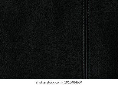 Texture of genuine black leather with a seam on the left side. Abstract monochrome background. A simple background of natural leather.