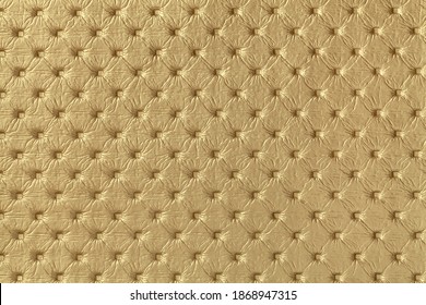 Texture of golden leather background with capitone pattern, macro. Yellow textile of retro Chesterfield style. Vintage fabric backdrop.