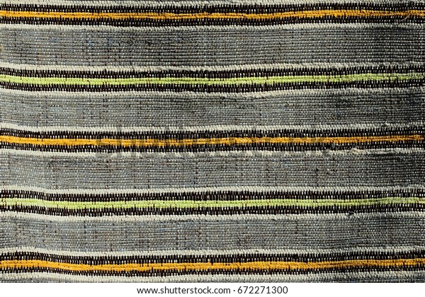 Texture of handmade carpet made on hand-loom,\
pattern of yellow, orange and black vertical lines dividing grey\
vertical fields