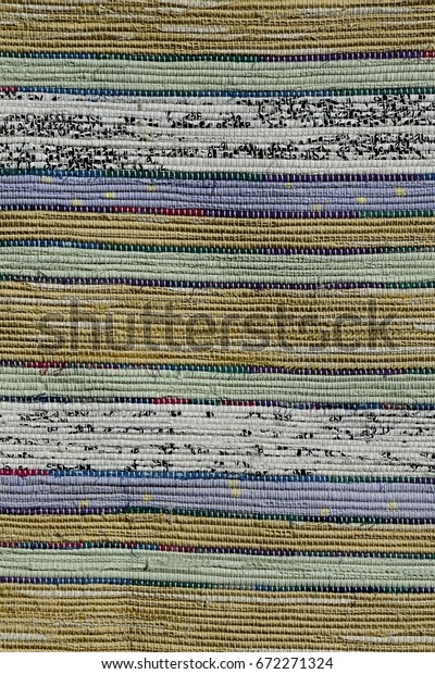 Texture of handmade carpet made on hand-loom,\
pattern of yellow, green, blue, white and black pastel vertical\
lines divided by thin black\
lines
