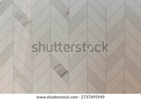 The texture of light beige rectangular ceramic tiles is laid in a herringbone pattern like parquet