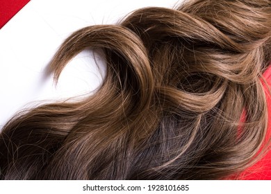 A texture of natural looking synthetic dark brown shiny wavy curly hair with highlights isolated on the white background