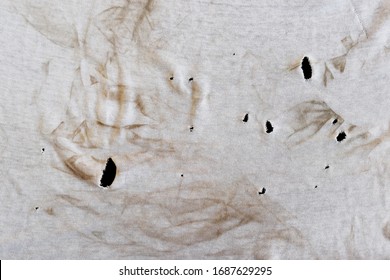 Texture of an old dirty ragged t shirt with brown stains. Dirty white fabric with many holes. Grunge damaged cloth on black background. Crumpled torn rag. Copy space