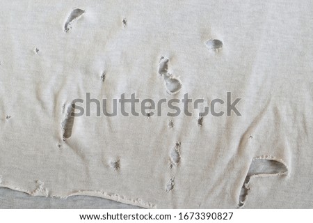 Texture of an old dirty ragged t shirt. Grunge damaged cloth for background.  Gray white fabric with holes. Crumpled torn rag