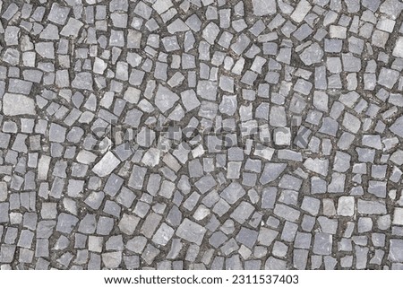 Texture of an old stoneblock pavement cobbled with gray stone tiles of different shapes as a background. Top view
