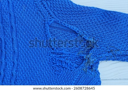 texture of old torn blue wool soft knitted patterned women's sweater with sleeves on gray wooden table