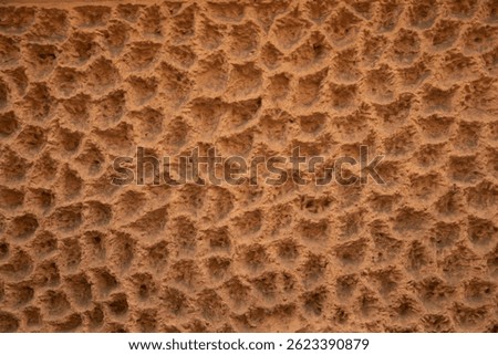 Texture of rough clay wall with characteristic pits and patterns, traditional construction technique in desert regions. Natural brown-orange color, effect of ancient handicraft
