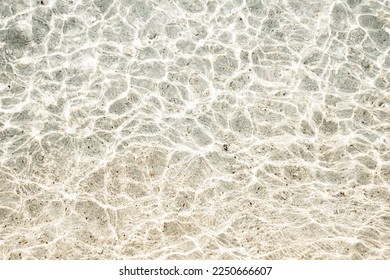 Texture of sand, pebbles and clearwater. Beautiful background, top view. The sun's rays shimmer on the water. - Shutterstock ID 2250666607