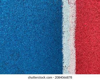 The texture of the surface of the rubber crumb of a sports field or playground in blue, red and a white stripe between them. Non-slip surface for sports and games - Shutterstock ID 2084066878