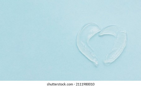 The Texture Of The Swatch Lip Balm In The Shape Of Heart. Transparent Ointment On Blue Background And Copy Space.