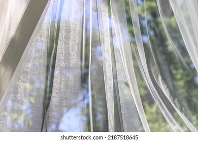 Texture Of A Wavy Surface Of A Chiffon Fabric Against A Blurry Green Trees And Blue Sky Outdoor Background