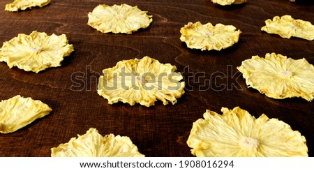 Texture of yellow fruit dried pineapple slices on dark brown wooden table.