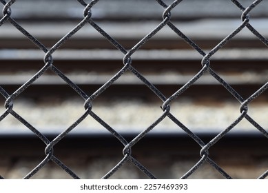 Textured black chain link fence. Abstract closeup with blurred railroad tracks in the background.