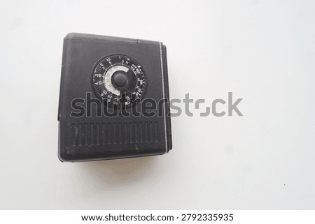 The textured black plastic casing of an old camera flash unit features a integrated manual calculator dial used to determine correct exposure settings for analogue photography.