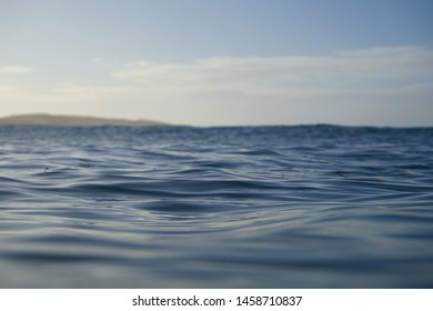 Textured blue water as a light breeze roughs up the surface of the ocean. Ripples cast dark shadows on the water giving the image depth. Taken from a water perspective as the sun sets