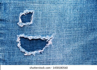 Textured denim background. Torn hole in the fabric. Blue tones