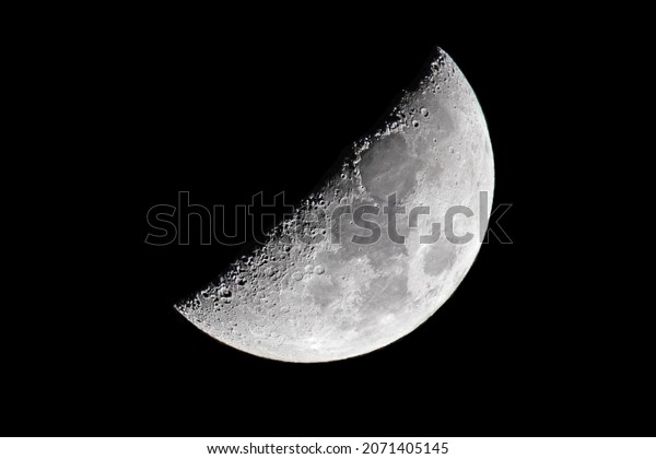 A textured gray\
half moon in a black sky