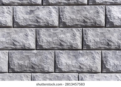 Textured grey split-face concrete blocks arranged in a running bond pattern. A seamless modular retaining wall with rustic, chiseled stone surfaces ideal for landscaping and architectural backdrops
