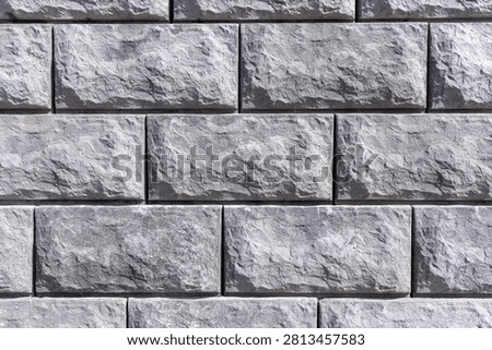Textured grey split-face concrete blocks arranged in a running bond pattern. A seamless modular retaining wall with rustic, chiseled stone surfaces ideal for landscaping and architectural backdrops