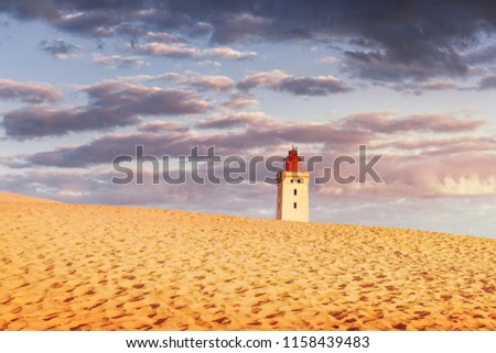 Textured sand dunes and light house in orange morning light and dramatic colorful sky. Rubjerg Knude Lighthouse, Lønstrup in North Jutland in Denmark, Skagerrak, North Sea 
