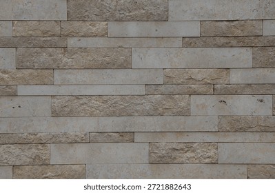 Textured stone wall composed of rectangular blocks in light beige and gray tones, highlighting natural variations and imperfections, perfect for design projects