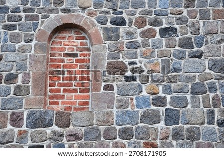 A textured stone wall featuring a red brick arch niche that has been bricked over.. Lubiń - Benedictine Abbey Monastery.