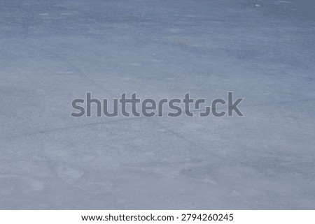 Textured surface of ice with light reflections and subtle color variations, indicating a cold winter environment with a clear sky
